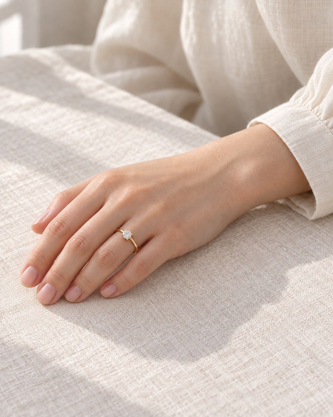 クリーム色の袖と、Veil Ringを着けた手元